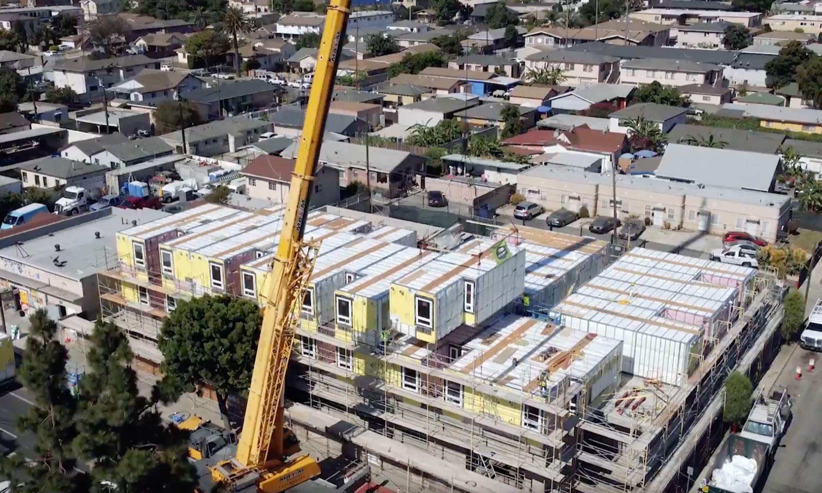 A tower crane setting volumetric modules onto the rising multi-story building.